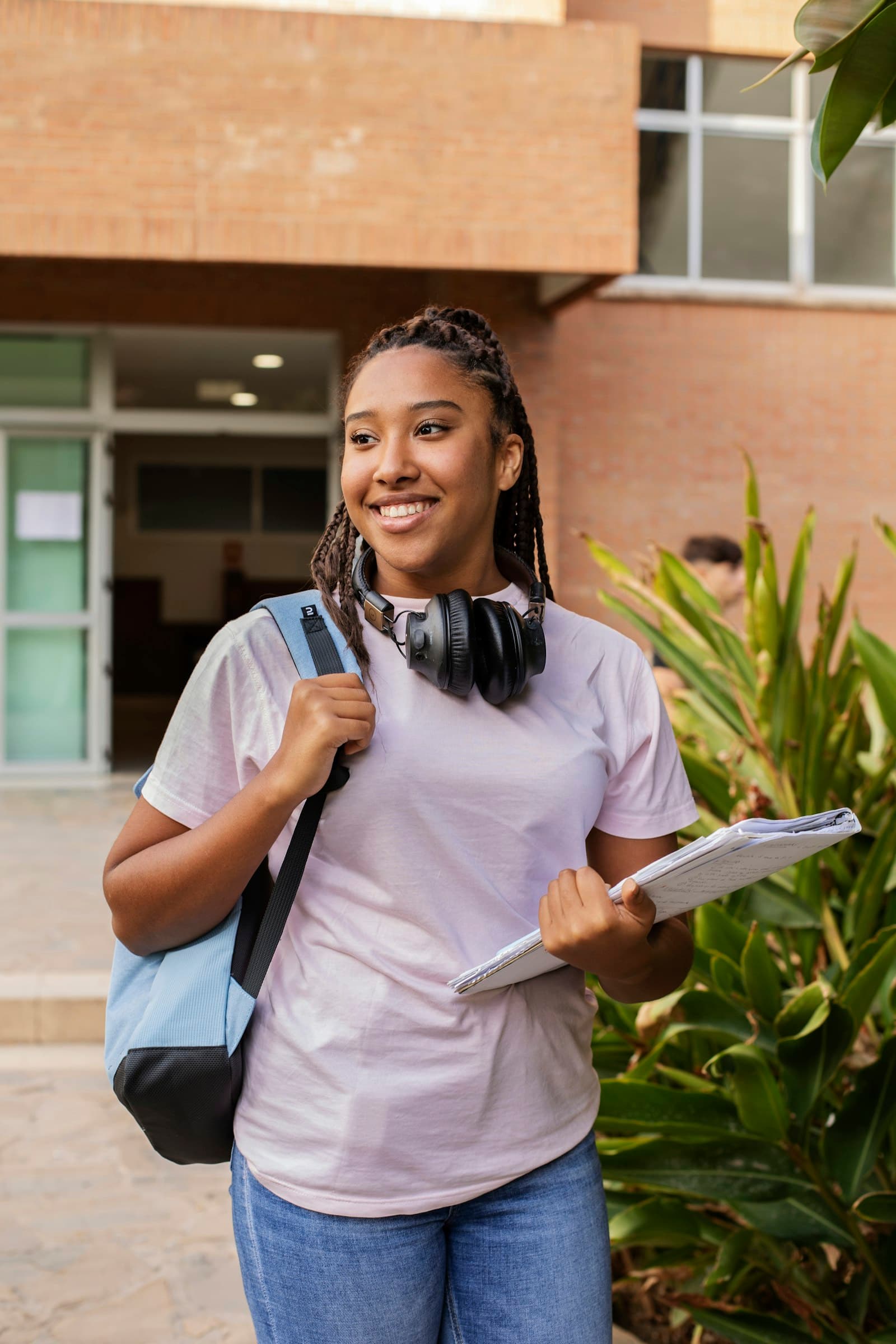 A smiling student with a backpack and notebooks walking across campus